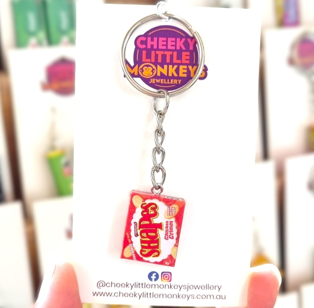 A novelty keychain shaped like an orange Arnott's Chicken Crimpy Shapes box, attached to a silver split ring and displayed on a white backing card branded 'Cheeky Little Monkeys Jewellery'.