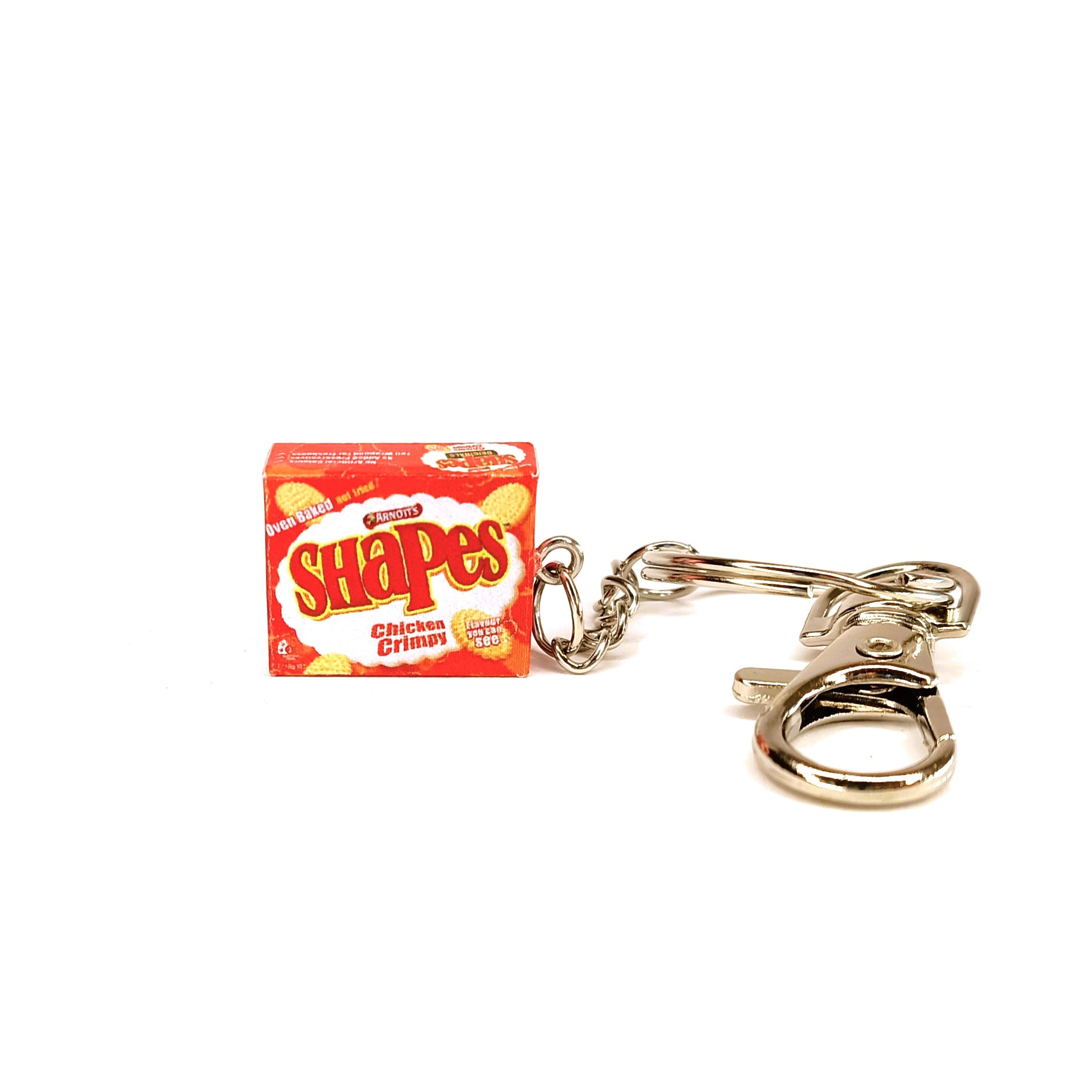A miniature keychain shaped like a box of Arnott's Chicken Crimpy Shapes , featuring an orange and yellow snack box design attached to a silver metal split ring and clasp, on a plain white background.