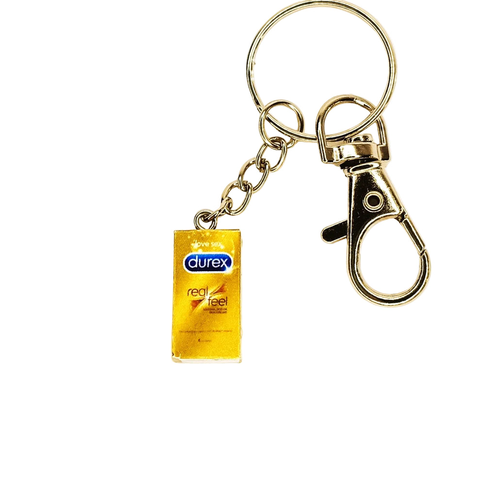 A novelty keychain featuring a miniature gold Durex Real Feel condom package charm attached to a silver metal split ring and lobster clasp, shown on a plain white background.