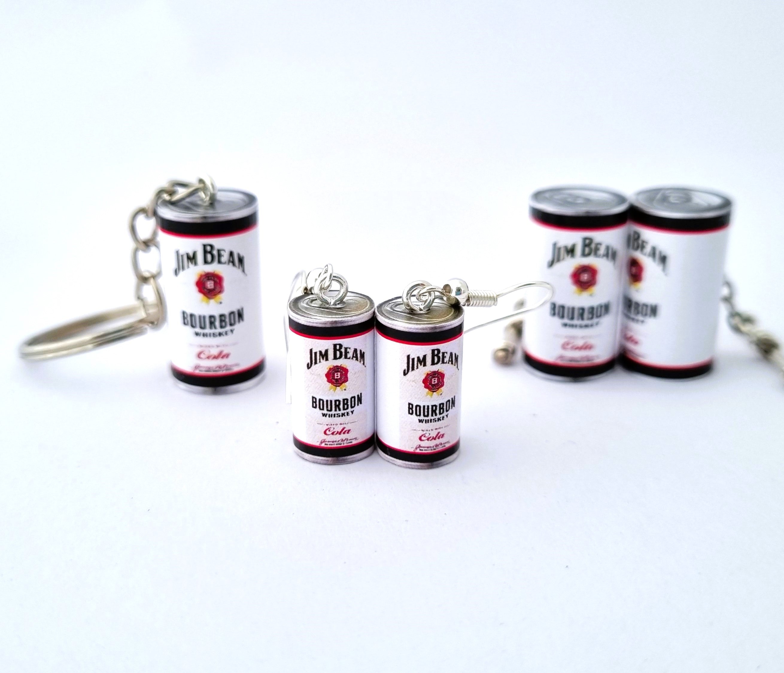 A set of miniature Jim Bean Bourbon whiskey bottle earrings on a clean white background with a miniature Jim Beam keyring behind and to the left and a pair of Jim Beam cufflinks behind and to the right.