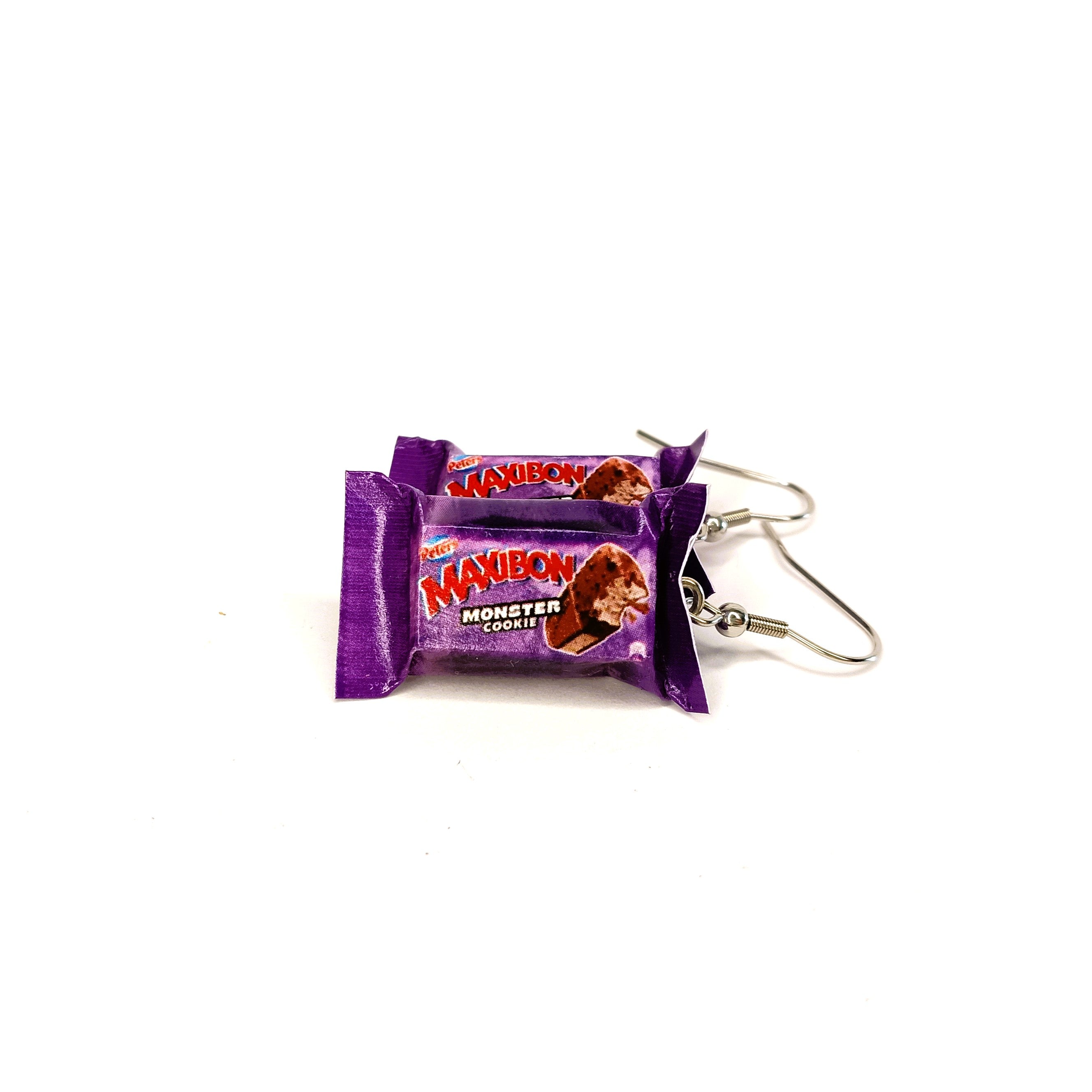 A pair of novelty earrings designed to look like two mini wrapped Maxibon Monster Cookie ice cream sandwiches, featuring purple wrappers and silver-tone fishhook ear wires, set against a plain white background.