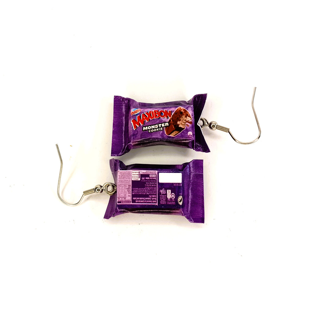 A pair of novelty earrings designed to look like miniature ice cream bars, featuring purple wrappers with 'Maxibon Monster Cookie' branding and silver-tone hook clasps, shown on a plain white background.