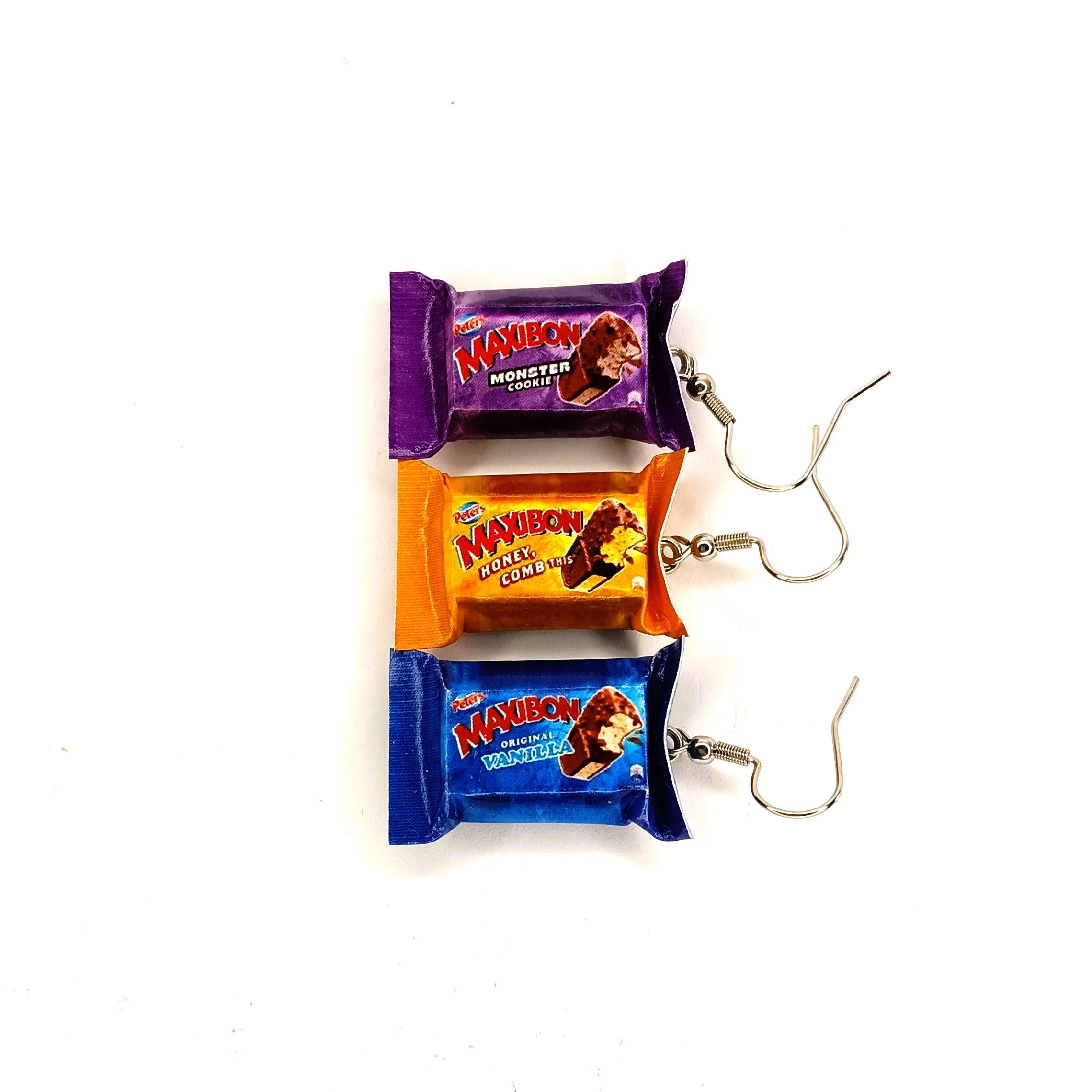 Three novelty earrings shaped like Maxibon ice cream sandwich bars, arranged vertically on a white background. The top earring is purple Monster Cookie with a silver hook, the middle is orange Honeycomb with a silver hook, and the bottom is blue Vanilla with a silver hook.