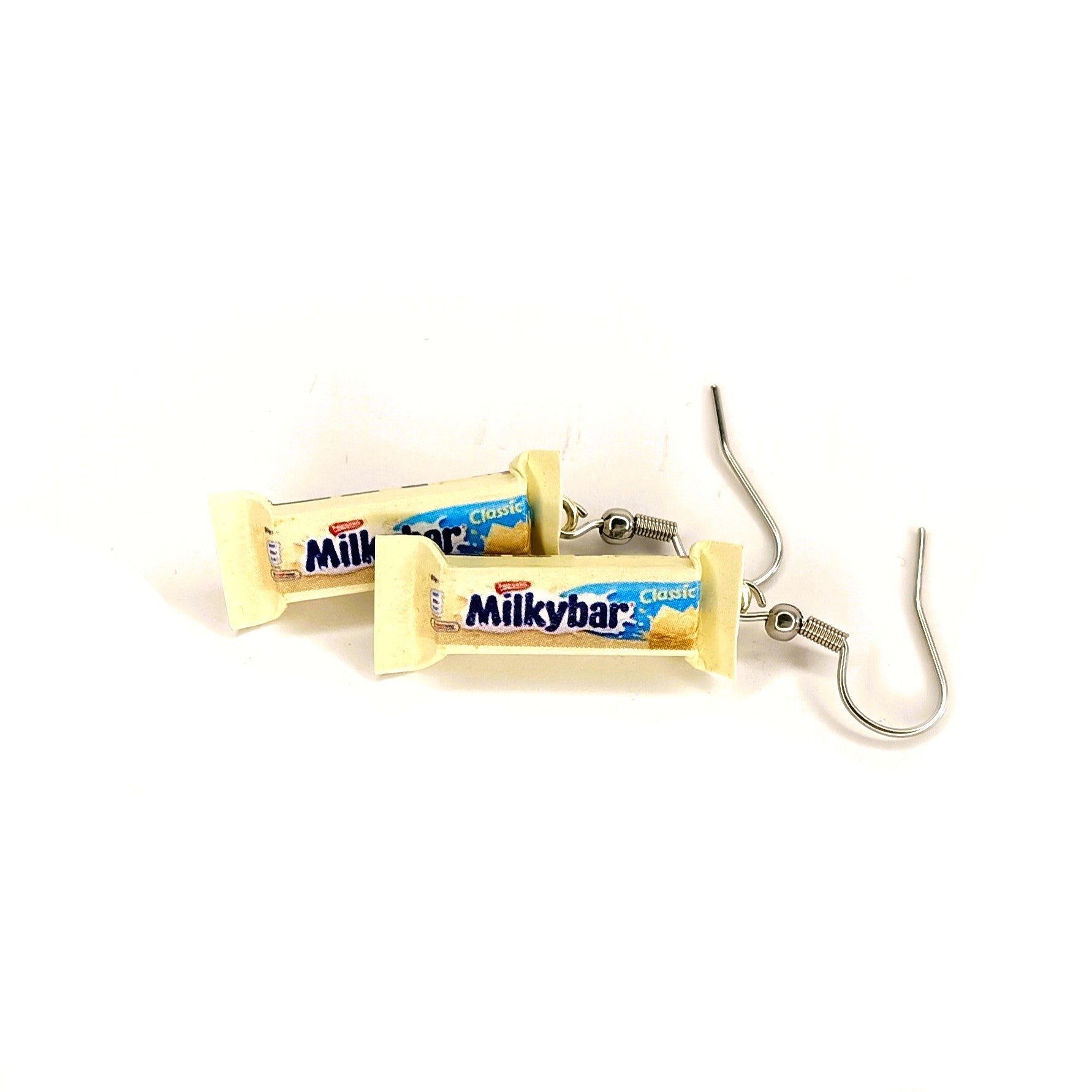 A pair of novelty earrings shaped like Milkybar chocolate bars, featuring the blue and cream candy bar packaging wrapped around silver-tone fishhook ear wires, shown on a plain white background.