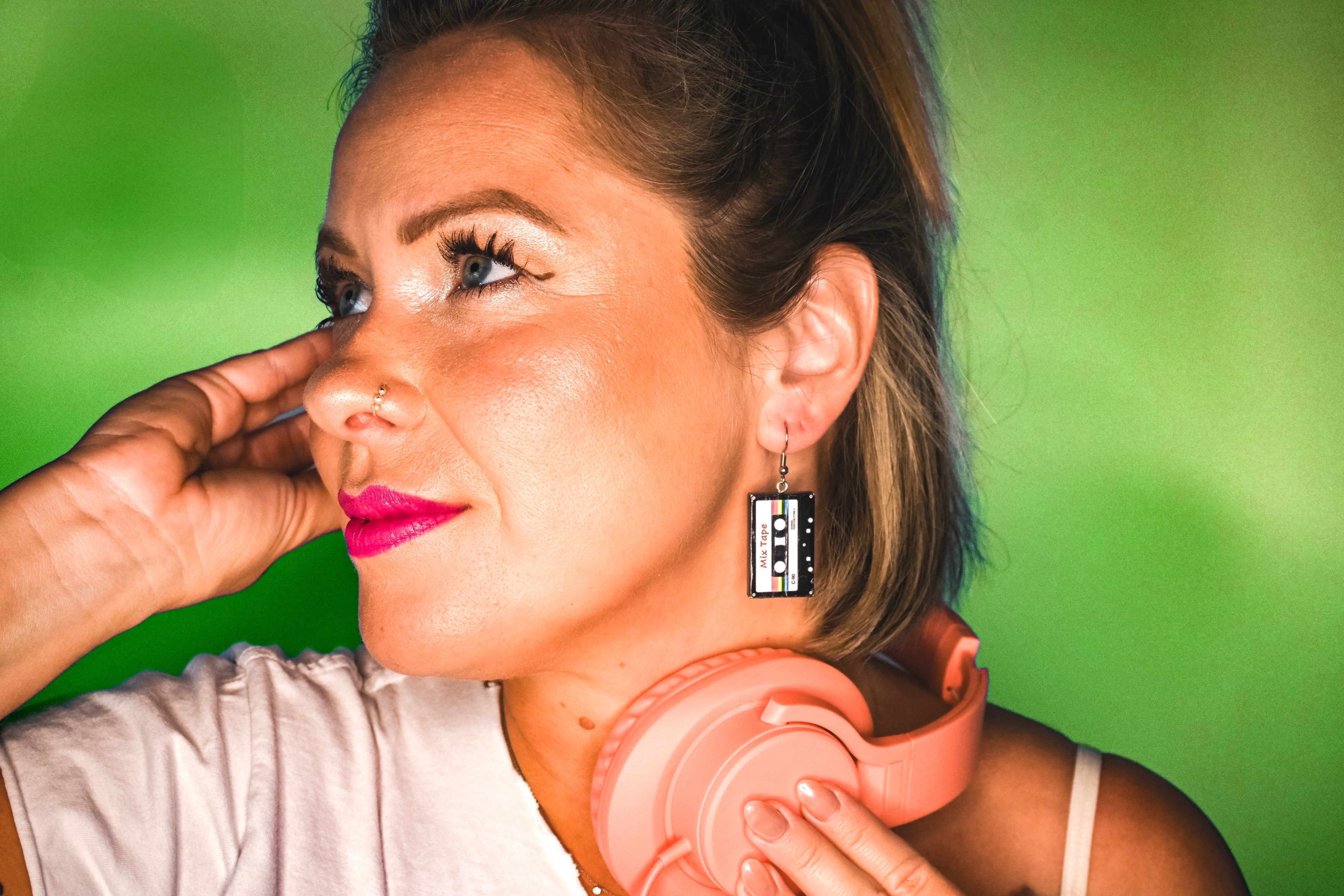 Woman wearing pink headphones and a unique Mix Tape earring against a green background