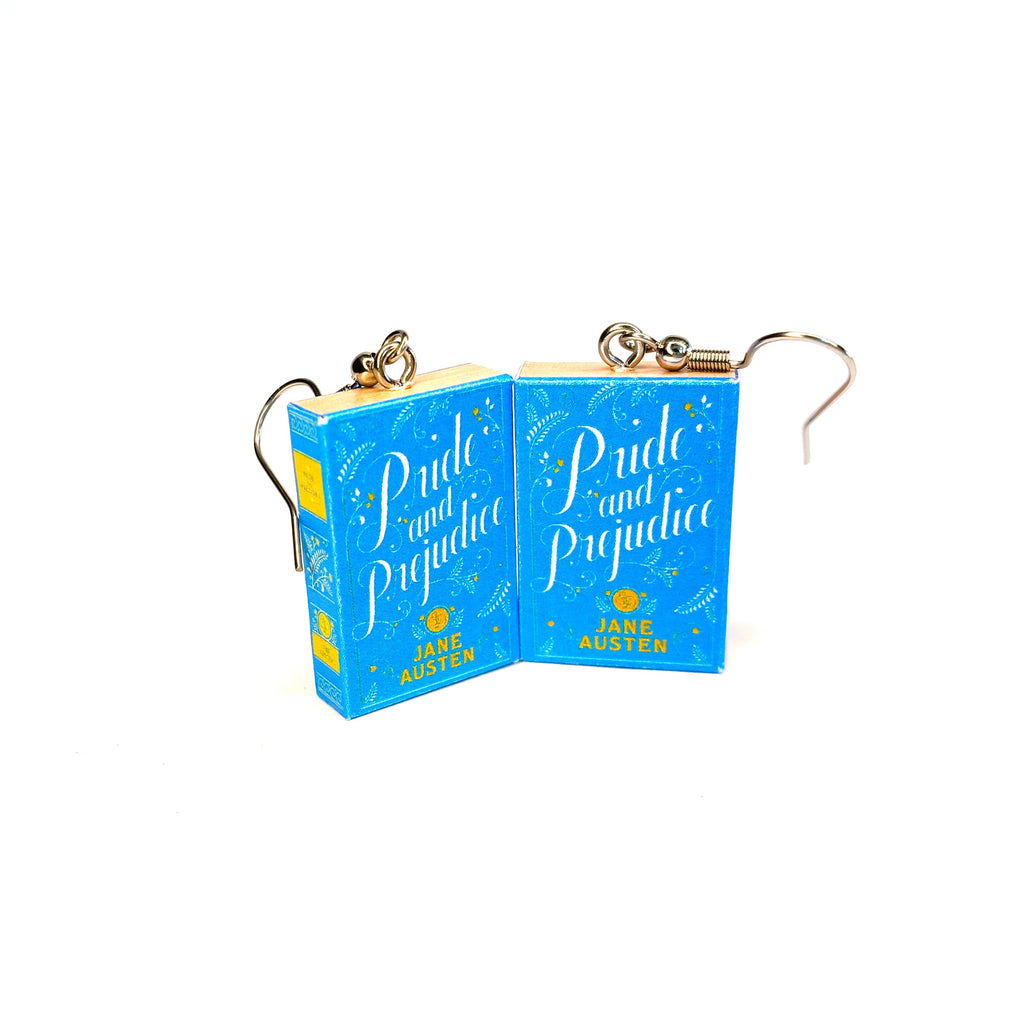A pair of earrings shaped like the book cover from the book 'Pride and Prejudice', featuring a bright blue cover design with gold accents and silver-tone fishhook wires, shown on a plain white background.