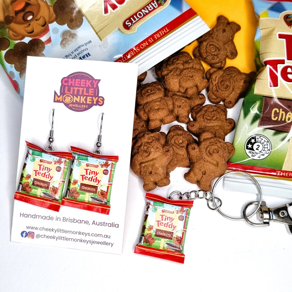 Cheeky Little Monkeys jewelry set featuring miniature 'Tiny Teddy' biscuit earrings and a matching keychain, displayed on a white card alongside teddy bear-shaped cookies and snack packaging.