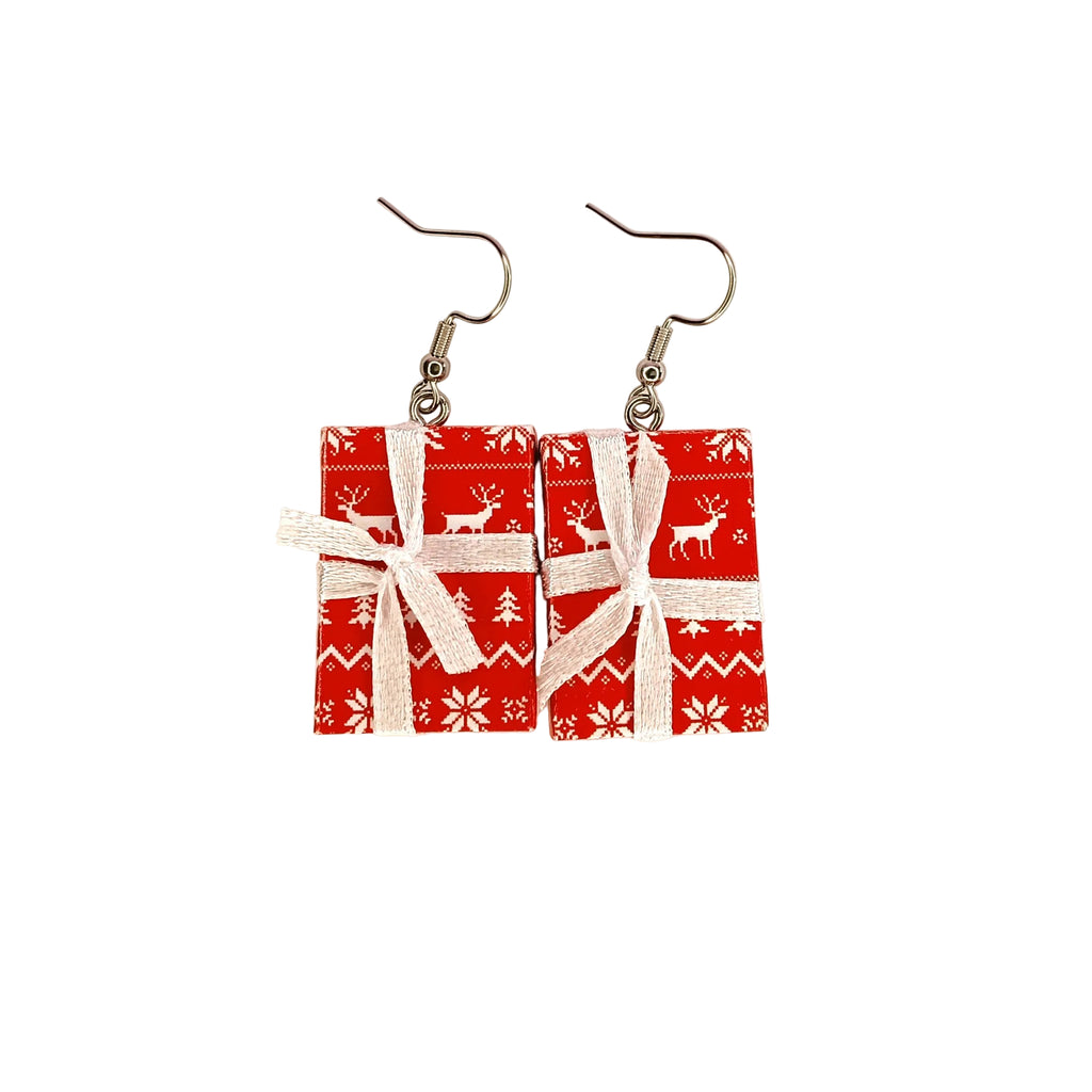 A pair of dangle earrings shaped like wrapped Christmas presents, featuring red gift boxes with white holiday patterns and white ribbon bows, suspended from silver fishhook ear wires on a plain white background.