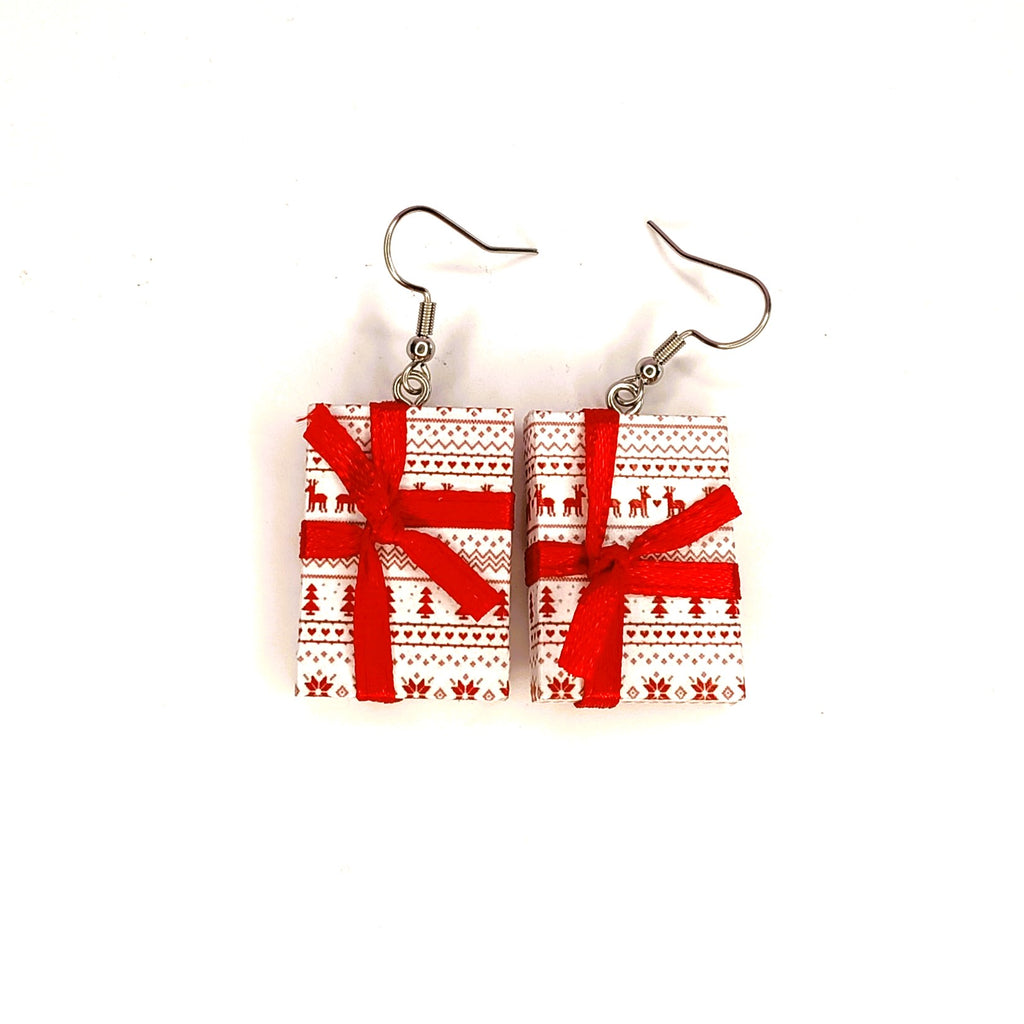 A pair of rectangular drop earrings shaped like wrapped Christmas presents, featuring a red and white Nordic pattern with red ribbon bows, hanging from silver fishhook wires on a plain white background.