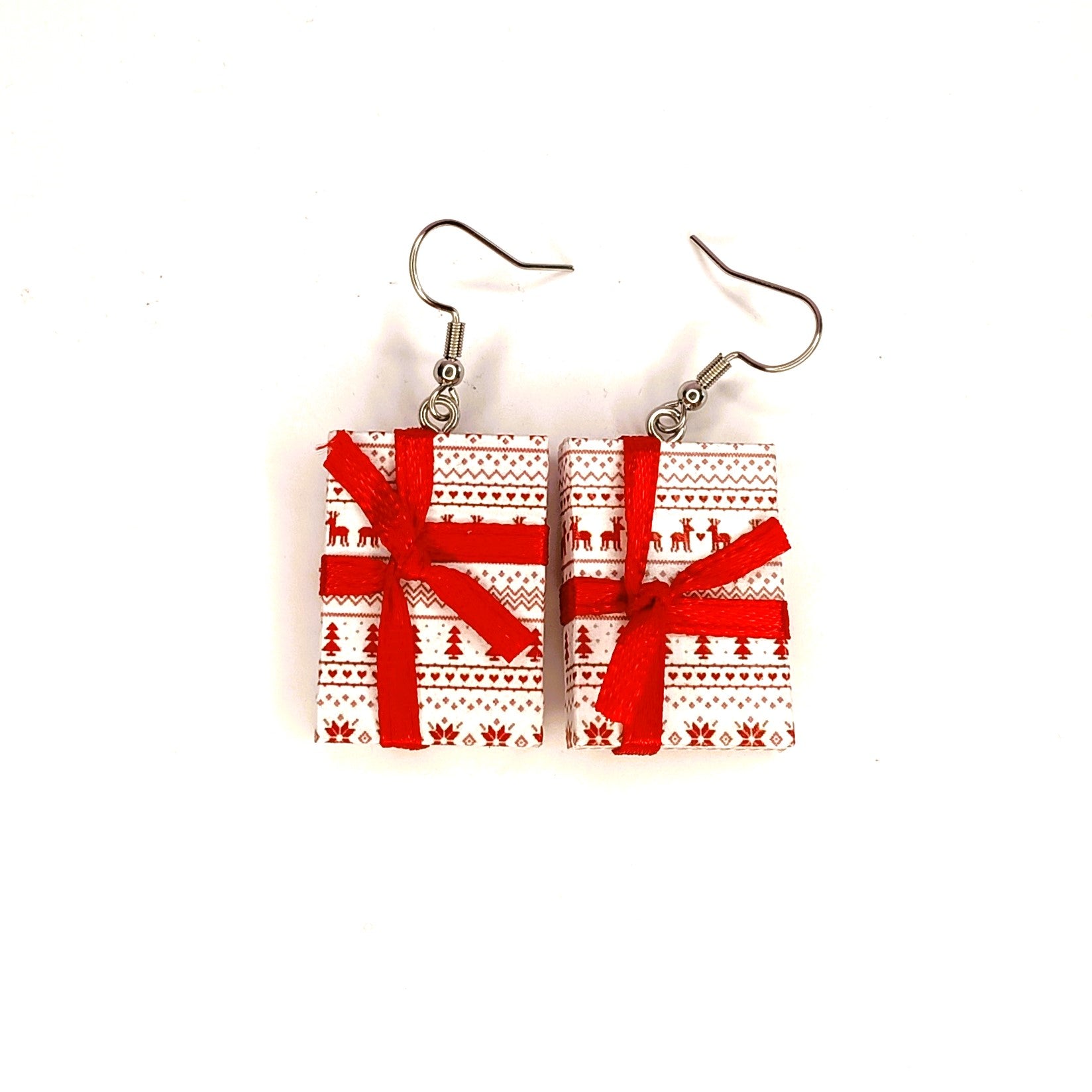 A pair of rectangular drop earrings shaped like wrapped Christmas presents, featuring a red and white Nordic pattern with red ribbon bows, hanging from silver fishhook wires on a plain white background.
